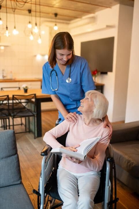 Care Home Nurse assisting elderly woman in wheelchair with reading.