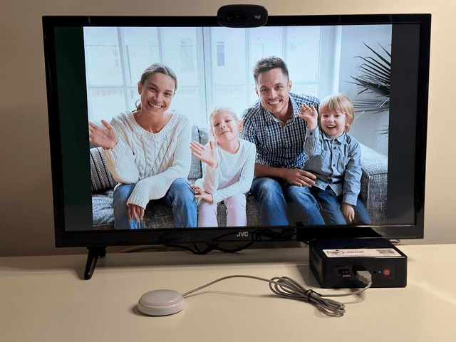 CallGenie device attached to television with the Do Not Disturb deactivated.  The button has no red light on and there is a family waving displayed on the screen
